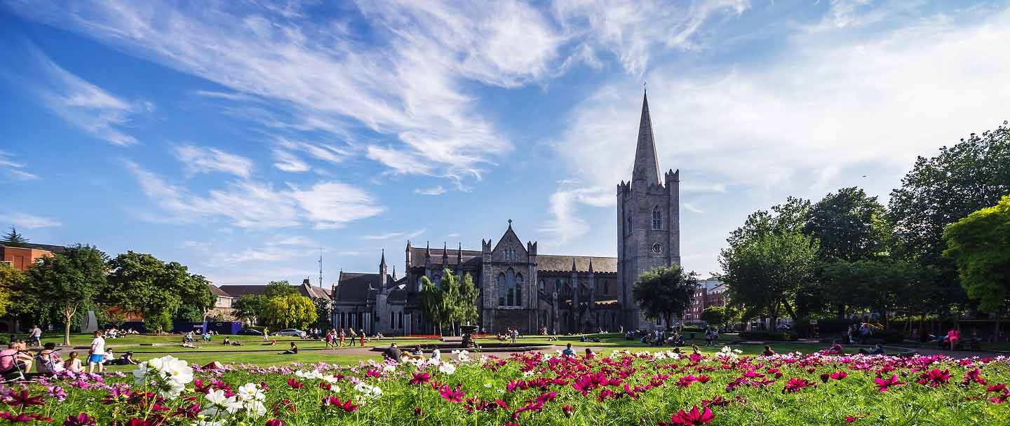 View of Trinity College Dublin with a flower-filled park in the foreground.