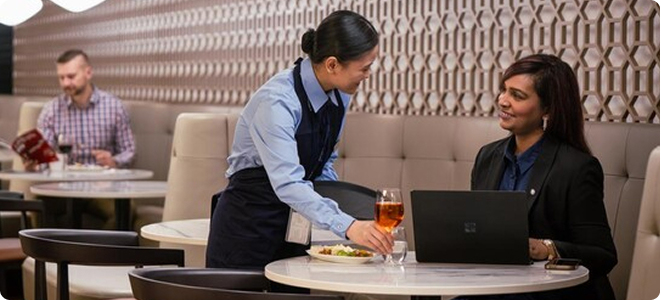 Woman being served glass of wine by a server in an airport lounge.