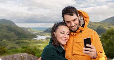 Two travelers taking a selfie with lush green hills in the background.