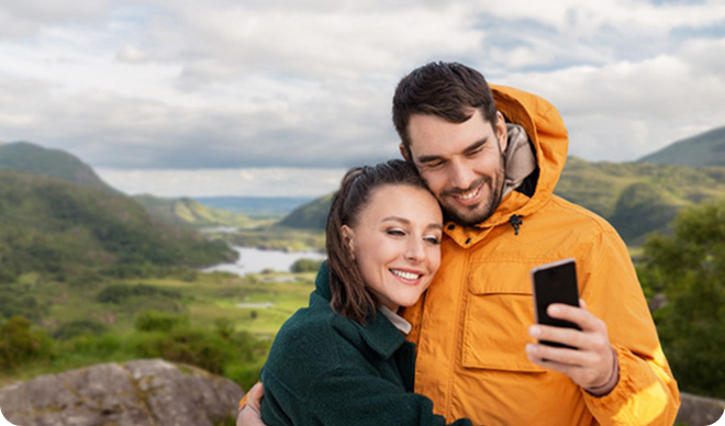 Two travelers taking a selfie with lush green hills in the background.
