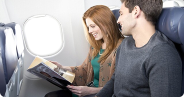 Travelers sitting in an airplane reading a magazine.