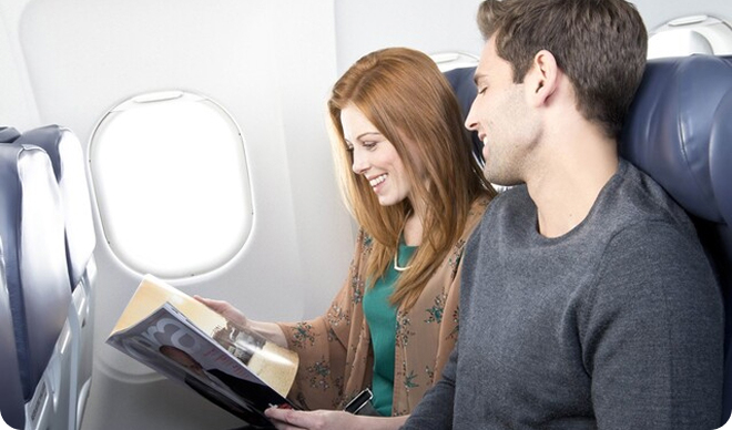 Travelers sitting in an airplane reading a magazine.