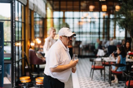 Guest holding drink near glass dining room.