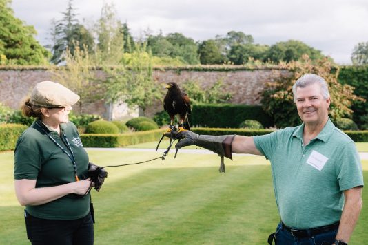 Falconer assisting attendee with bird on glove.
