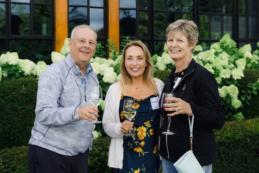 Three attendees posing with drinks outdoors.