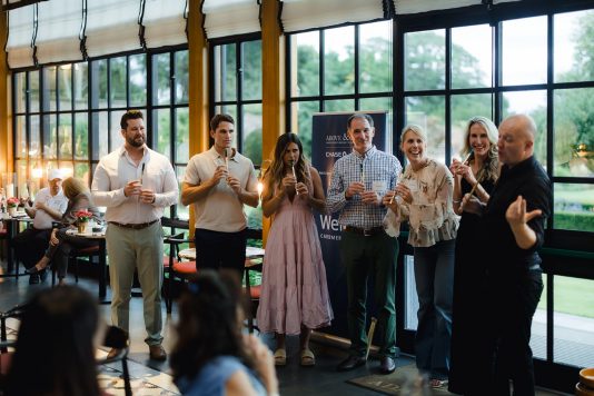 Group of guests standing and listening indoors.