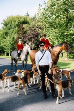 Riders on horseback leading a group of dogs.