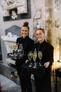 Servers carrying trays of champagne glasses.