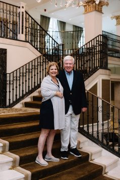 Two guests posing on an indoor staircase with railing.