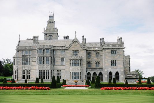 Front view of Adare Manor with lawn and flowers.