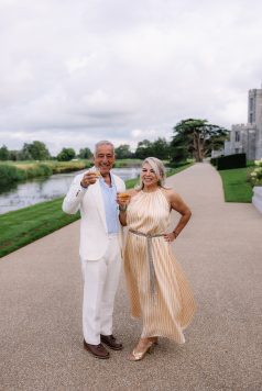 Two guests holding drinks on a path near water.