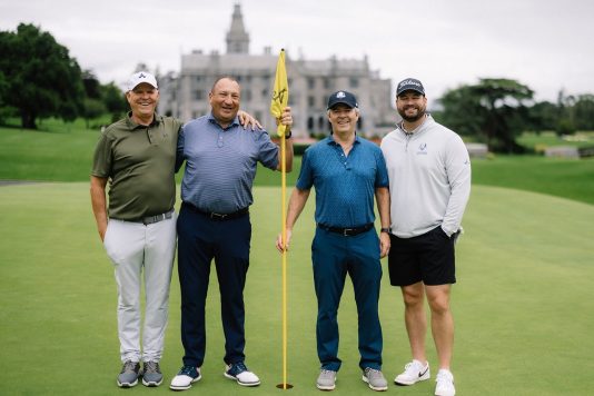 Group of four guests posing with a golf flag.