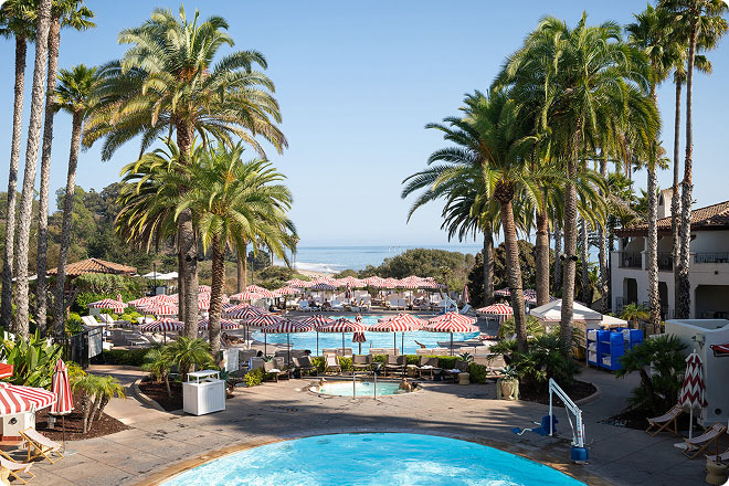 Resort pool surrounded by palm trees with ocean views in the distance