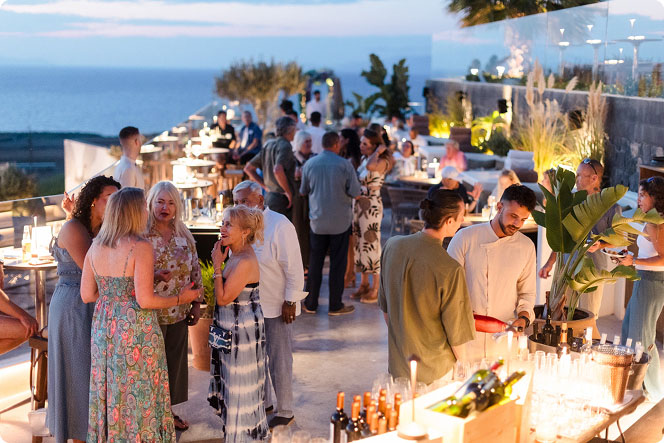 Group of guests mingling at an outdoor evening reception with tables and coastal views