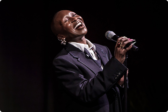 Performer singing into a microphone on a dimly lit stage during a live music performance