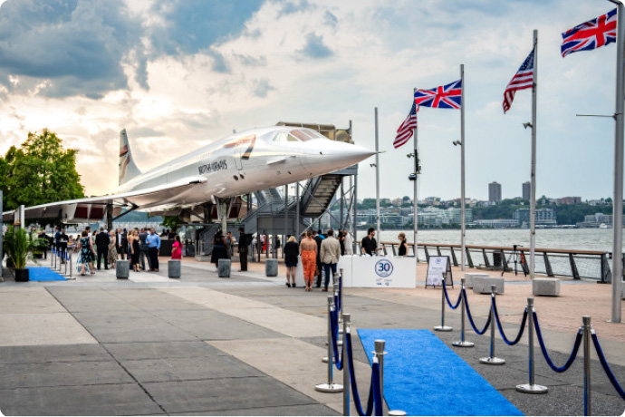 Concorde aircraft on display at an outdoor pier with visitors walking along a blue carpet and flags nearby