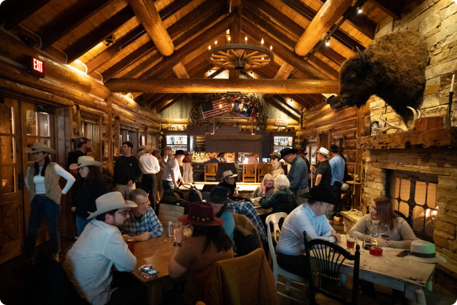 Large group seated inside a rustic lodge dining hall with wooden beams, warm lighting, and mounted décor