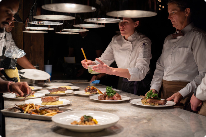 Chef plating gourmet dishes in a professional kitchen with multiple plates arranged on a counter