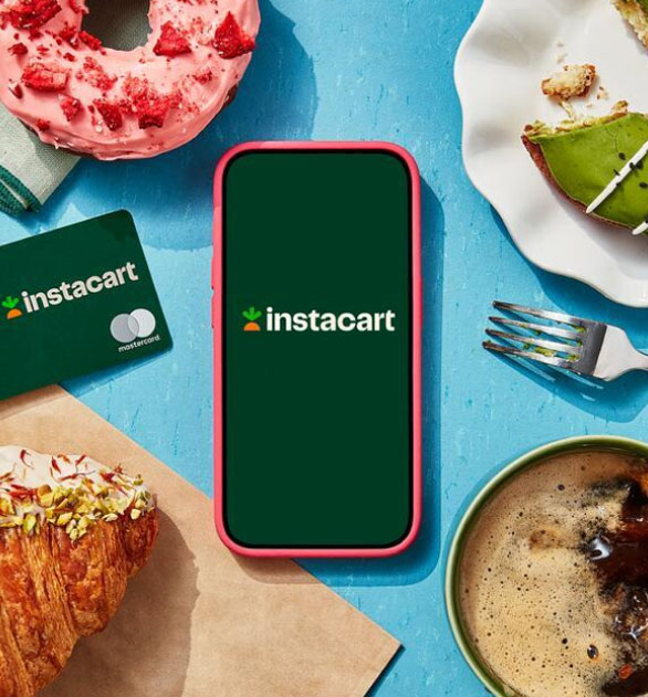 Overhead shot of smartphone with Instacart logo onscreen, surrounded by the Instacart Mastercard, colorful pastries, and a coffee.