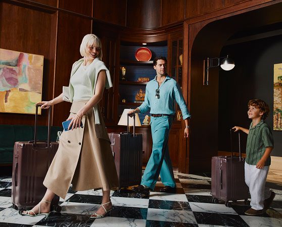Travelers walking through a hotel lobby with rolling luggage.