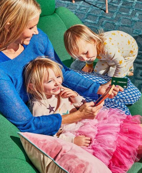 A mother with her two young kids making a purchase on a smartphone with their Instacart Mastercard.